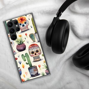 Może przedstawiać: Przezroczyste etui na telefon z białym tłem i kolorowym wzorem przedstawiającym czaszki cukrowe, kaktusy i kwiaty. Wzór jest inspirowany meksykańskimi tradycjami Dnia Zmarłych.