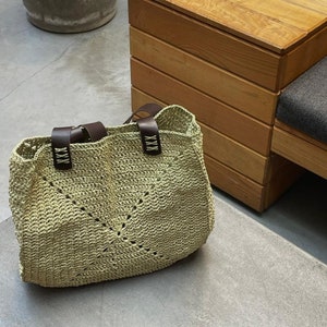 May include: A light green crocheted tote bag with brown leather straps and the word "XXX" embossed on the straps.