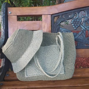 May include: A green crocheted tote bag with a matching crocheted sun hat. The bag has a long strap and a small pocket on the front. The hat is folded and placed on top of the bag.