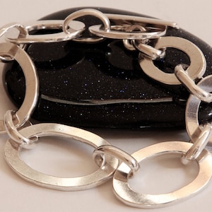May include: A silver bracelet with large oval links. The bracelet is resting on a black stone.
