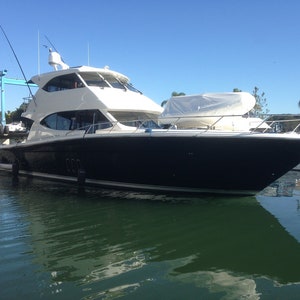 Könnte beinhalten: Eine große, schwarz-weiße Motoryacht, die in einem Yachthafen angelegt ist. Das Boot hat eine weiße Kabine mit einer großen Windschutzscheibe und einen schwarzen Rumpf. Das Boot liegt im Wasser mit blauem Himmel im Hintergrund.