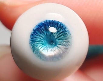 Puede incluir: Primer plano de un ojo de vidrio azul y blanco con un iris detallado y una esclerótica blanca.