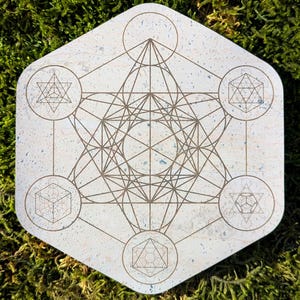 Könnte beinhalten: Ein weißer sechseckiger Korkuntersetzer mit einem braunen geometrischen Design. Das Design besteht aus einer Reihe von sich überlappenden Kreisen und Linien, die ein komplexes und filigranes Muster bilden.