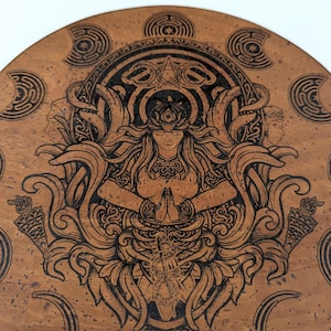 May include: A circular cork coaster featuring a dark laser-engraved illustration of a central figure with hands pressed together in prayer, surrounded by intricate swirling foliage, torches, and crescent moon symbols arranged in a circular border.