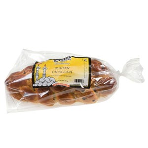 May include: A braided loaf of raisin challah bread in a clear plastic bag. The label reads "Traditional Raisin Challah" with a graphic of two candle holders. The bread is a golden brown color with dark raisins visible throughout.