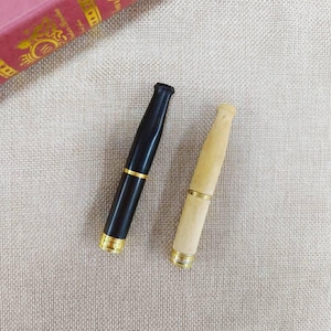 Puede incluir: Dos porta cigarrillos, uno negro y otro de madera natural, con detalles dorados.