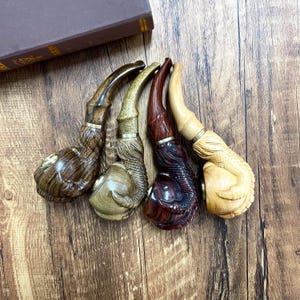 May include: Four wooden smoking pipes with intricate carvings. The pipes are in various shades of brown, beige, and dark red. The pipes are arranged in a row, with the bowls facing the viewer.