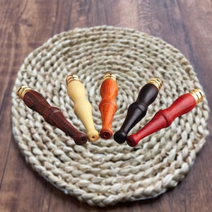 May include: Five wooden cigarette holders with gold metal tips. The holders are in different colors: brown, beige, orange, black, and red.