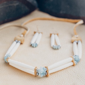 May include: A white bone necklace with light blue gemstone accents and matching earrings. The necklace has a double strand of bone beads and a cluster of gemstones in the centre.