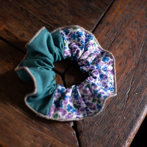 May include: A teal and floral patterned scrunchie with a gray trim. The scrunchie is made of fabric and is tied in a knot.