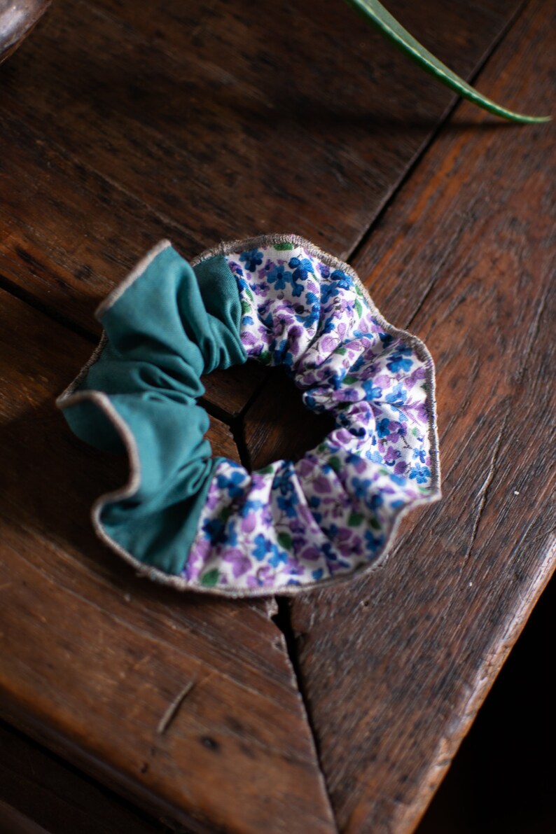 May include: A teal and floral patterned scrunchie with a gray trim. The scrunchie is made of fabric and is tied in a knot.