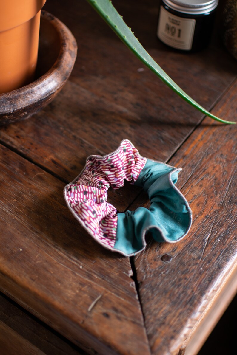 May include: A teal and pink fabric scrunchie with a white and red geometric pattern.