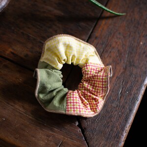 May include: A handmade fabric hair scrunchie with a yellow and white checkered pattern, a green fabric section, and a red and white checkered pattern.