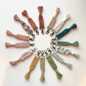 Può includere: Una collezione di 15 portachiavi in macramè colorati con nappe. I portachiavi sono realizzati con filati di diversi colori e presentano una varietà di motivi.
