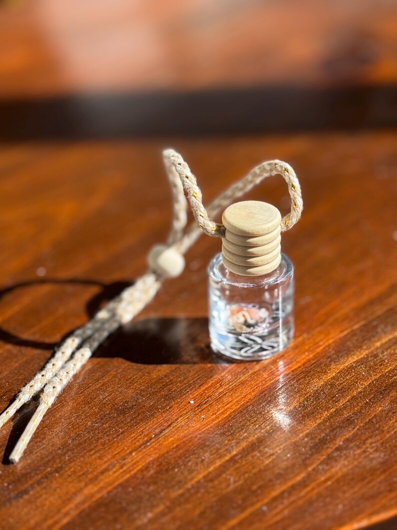 May include: A small glass bottle with a wooden lid and a string attached. The bottle is filled with a clear liquid and small, colorful objects.