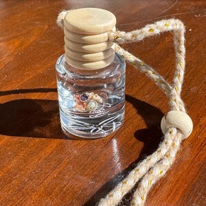 May include: A clear glass bottle with a wooden lid and a beige rope attached. The bottle contains small, colorful stones and is designed to be hung in a car.