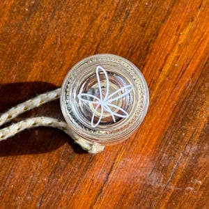 May include: A clear glass bottle stopper with a white floral design. The stopper has a rope attached to it.