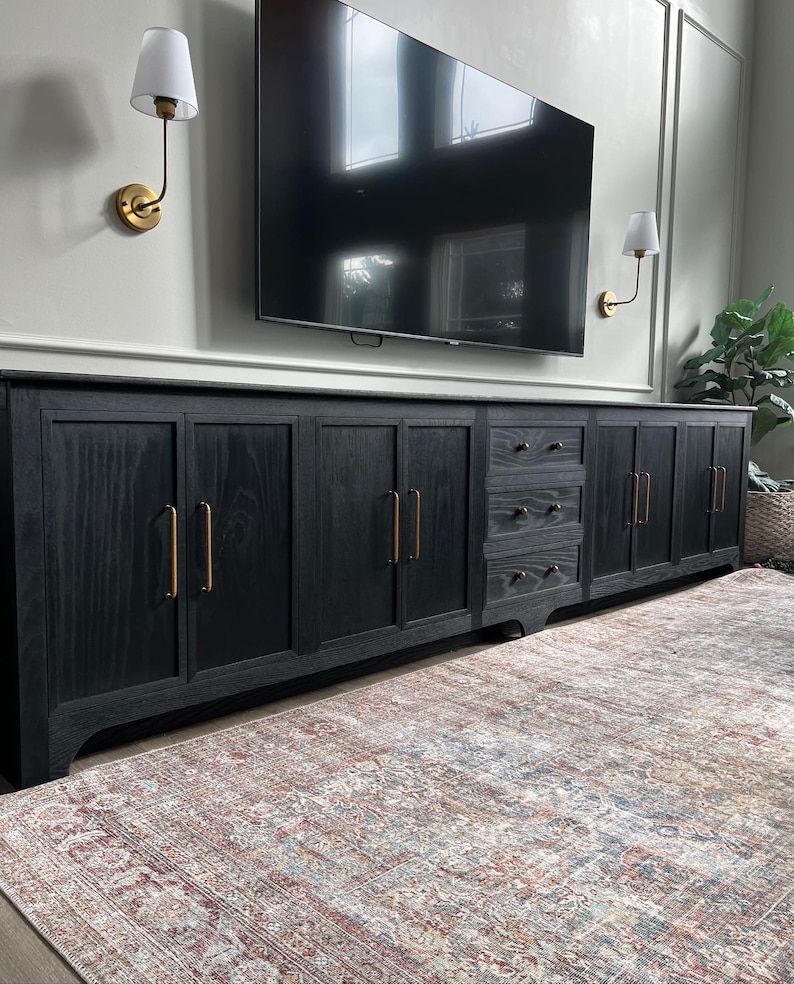 May include: A black wooden media console with multiple doors and drawers. The console has gold hardware and sits on a patterned rug.