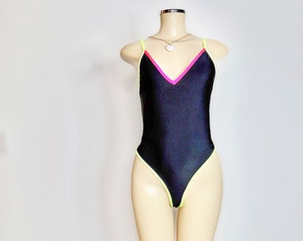 May include: Black swimsuit with neon green and pink trim. The swimsuit has a V-neck and a high leg cut.