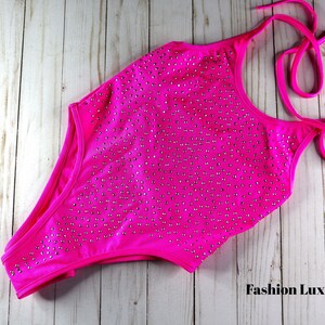 May include: A vibrant fuchsia one-piece swimsuit with a halter neck and high-cut leg. The swimsuit is embellished with numerous small, silver-colored rhinestones. The words "Fashion Lux Shop" are visible in the bottom right corner.