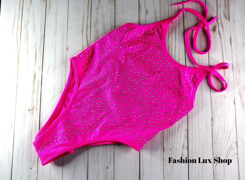 May include: A vibrant fuchsia one-piece swimsuit with a halter neck and high-cut leg. The swimsuit is embellished with numerous small, silver-colored rhinestones. The words "Fashion Lux Shop" are visible in the bottom right corner.