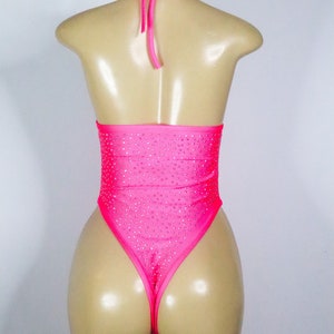 May include: A hot pink bodysuit with a halter neck and high-cut leg. The garment is embellished with small, sparkling rhinestones. The mannequin is displayed against a plain white background. The text "Fashion Lux Shop" is visible at the bottom.
