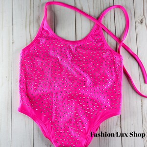 May include: A hot pink swimsuit with silver embellishments. The one-piece swimsuit has a halter neck design and tie straps. The swimsuit is covered in small, silver-colored studs. The text "Fashion Lux Shop" is visible on the bottom right.