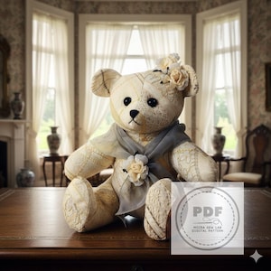 Può includere: Un orsacchiotto color crema con dettagli floreali e una sciarpa grigia. L'orso ha occhi neri a bottone ed è seduto su una superficie di legno. L'orso indossa un vestito color crema con dettagli floreali. L'immagine include un logo PDF.