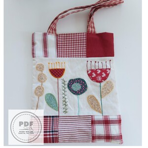 Puede incluir: Bolso tote patchwork con dise&ntilde;o floral. El bolso presenta un fondo blanco con flores bordadas en rojo, azul y beige. Las asas y el borde superior son de tela a cuadros rojos y blancos. El bolso tiene un logotipo PDF.