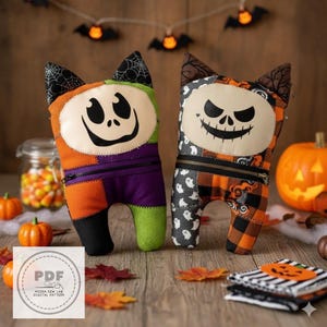 Può includere: Due bambole di gatto di peluche a tema Halloween con disegni patchwork. Una bambola è arancione, verde e viola con una faccia sorridente. L'altra è nera, bianca e arancione con una faccia di teschio. Le bambole hanno orecchie di gatto nere.