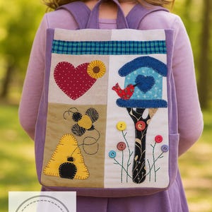 May include: A patchwork backpack with a whimsical design. The front features a heart, sunflower, birdhouse, bee, and beehive appliqu&eacute;s. The backpack has a purple exterior and a plaid fabric accent at the top. The design includes colourful buttons and embroidered details.
