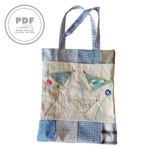 Puede incluir: Un bolso tote crema con detalles y asas de patchwork azul y blanco. La bolsa presenta dise&ntilde;os florales bordados y formas triangulares. El texto "PDF MOIRA SEW LAB DIGITAL PATTERN" est&aacute; en un c&iacute;rculo en la parte superior izquierda.
