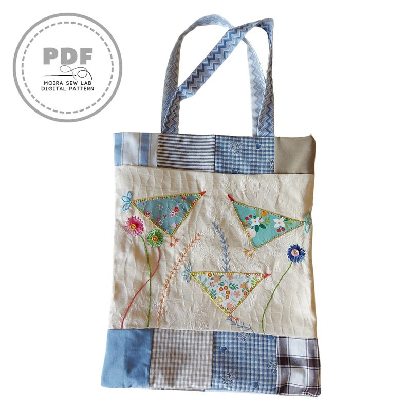 Puede incluir: Un bolso tote crema con detalles y asas de patchwork azul y blanco. La bolsa presenta dise&ntilde;os florales bordados y formas triangulares. El texto "PDF MOIRA SEW LAB DIGITAL PATTERN" est&aacute; en un c&iacute;rculo en la parte superior izquierda.