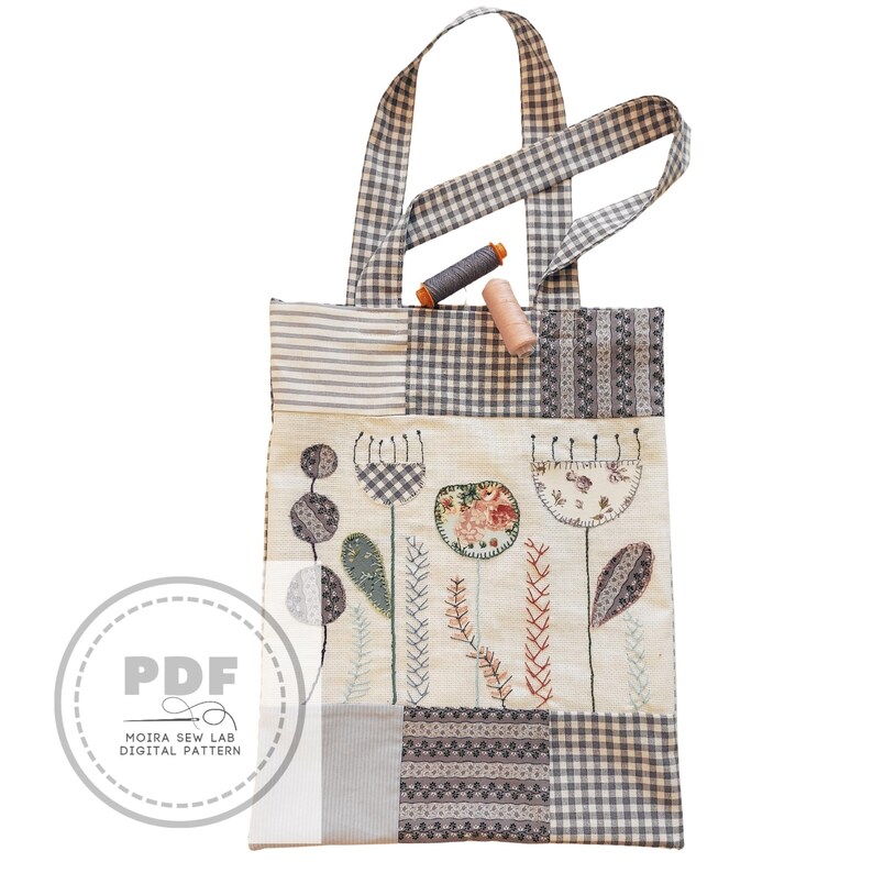 Puede incluir: Un bolso tote patchwork con un dise&ntilde;o floral y asas de cuadros. El bolso presenta flores bordadas y patrones geom&eacute;tricos en tonos neutros. Dos carretes de hilo descansan en el borde superior. El bolso tiene un logotipo "PDF".