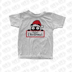 Puede incluir: Una camiseta gris con un gato negro que lleva un gorro de Papá Noel rojo asomándose por encima de un cartel rojo que dice "MEOWY Christmas".
