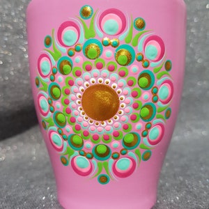 Puede incluir: Una taza de cerámica rosa con un diseño de mandala pintado a mano. El mandala presenta puntos y círculos verdes, azules, rosas y dorados.