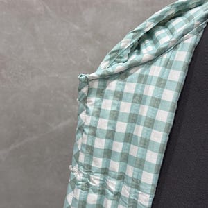 K&ouml;nnte beinhalten: Nahaufnahme eines gr&uuml;n-wei&szlig;en Gingham-Stoffes mit einer Naht an der Seite.
