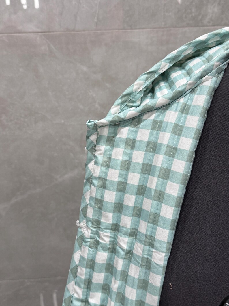 K&ouml;nnte beinhalten: Nahaufnahme eines gr&uuml;n-wei&szlig;en Gingham-Stoffes mit einer Naht an der Seite.