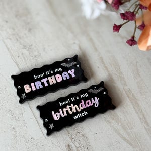 May include: Two black rectangular birthday-themed decorations. One reads "boo! It's my BIRTHDAY" in a gradient of pink and purple. The other says "boo! It's my birthday witch" in a similar gradient. Both have bat and star accents.