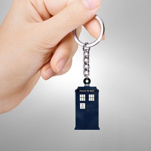 May include: A blue keychain featuring the iconic British police box, the TARDIS, from the Doctor Who series. The keychain has a silver chain and ring. The words "POLICE BOX" are visible on the top of the box.