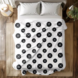 May include: White bedspread with a repeating pattern of black circles, each containing a stylized white "X" symbol. The bedding is on a bed with white pillows. The overall theme is a modern, minimalist design.