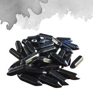 May include: A pile of black obsidian arrowhead points. The points are smooth and polished, with a sharp tip. The points are arranged in a random pattern, with some overlapping.