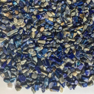 May include: A close-up of a pile of small, blue and gray lapis lazuli chips. The chips are irregular in shape and size, and some have a metallic sheen.