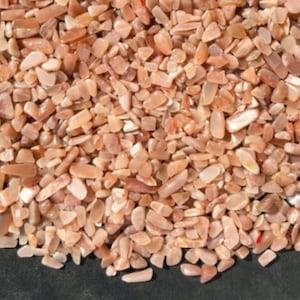 May include: A close-up of a pile of small, pink sunstone chips. The chips are various shapes and sizes, with a shimmery, iridescent finish.