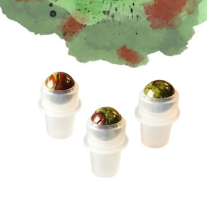 May include: Three roll-on bottles with gemstone tops. The gemstones have a mix of red, brown, and green colours. The bottles are white and have a clear roller ball. The background has a watercolour design with green and red hues.