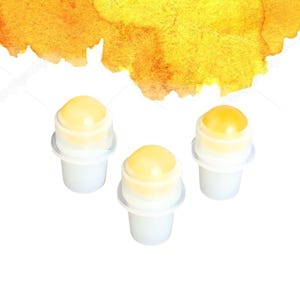 May include: Three small, white containers with a yellow, rounded top. The tops are a lighter yellow colour and appear to be a gel or balm. The background features a watercolour wash of yellow and orange.