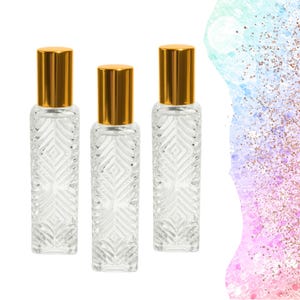 Può includere: Tre flaconi di profumo in vetro trasparente con tappi color oro. I flaconi hanno una forma rettangolare con un motivo strutturato a forma di diamante. Lo sfondo è bianco con un design colorato e glitterato sul lato destro.