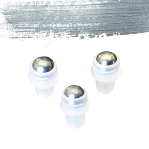 May include: Three clear plastic rollerball bottles, each with a shiny, silver metal ball applicator. They are set against a white backdrop with a grey brushstroke design in the upper left. These are likely for essential oils or cosmetic products.