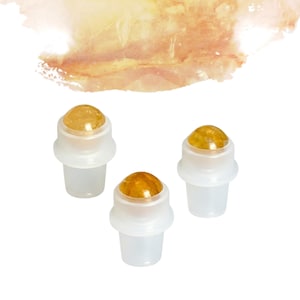 May include: Three clear glass roll-on bottles with amber-coloured tops. The bottles have a white base and a rounded top. The background is white with a watercolour wash of orange and yellow.