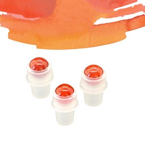 May include: Three clear plastic roller bottles with red, spherical tops. The bottles are arranged in a triangular pattern against a white background. An orange watercolour design is in the upper portion of the image.